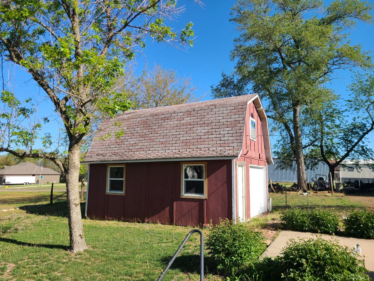 Small red barn with old shingle roof before metal roof replacement